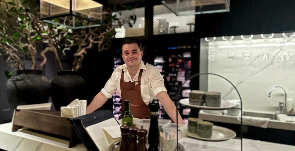 Mann med forkle i vinbar som lener seg p&aring; disken