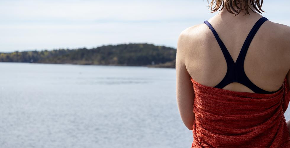 Et bilde av en dame i badedrakt og h&aring;ndkle tatt bakfra i forgrunnen Viser Oslofjorden i bakgrunnen.