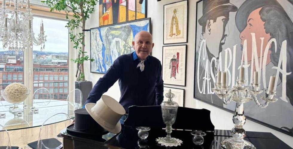 En mann bak et piano med malerier, et glassbord og vindu med utsikt ut mot Oslo bak han.