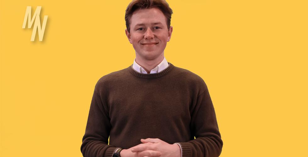 Mann i brun genser st&aring;r foran en gul green screen bakgrunn.