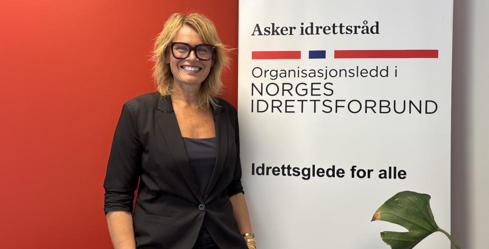 Gry Elisabeth Garlie, daglig leder i Asker idrettsr&aring;d, ved siden av en plakat