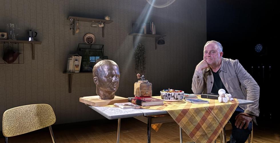 En mann og en byste av en annen mann på sitter på et bord. 