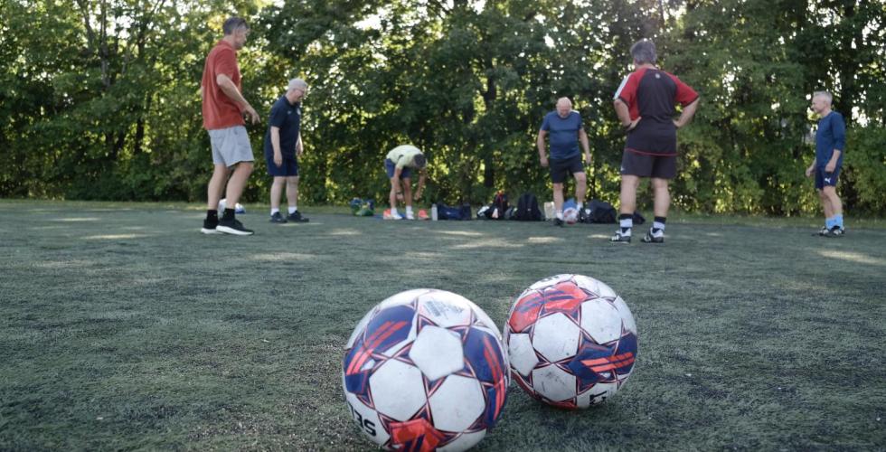 To fotballer i forgrunnen hvor de i bakgrunnen gjør seg klar for trening