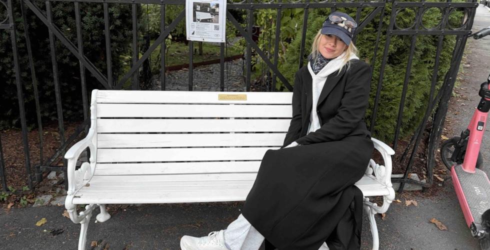 En jente iført en svart kåpe sitter på frognerbenken