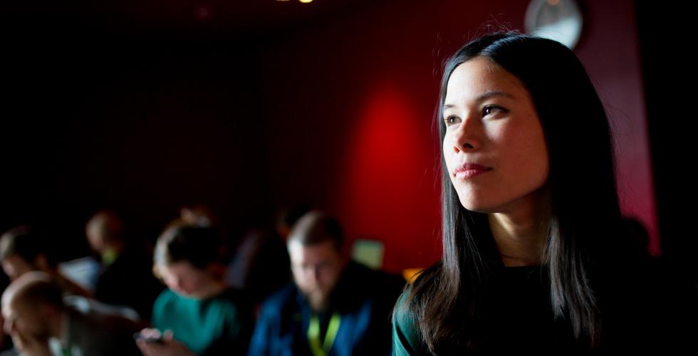 Dame med mørkt hår i forgrunnen til høyre i bildet og flere folk i bakgrunnen