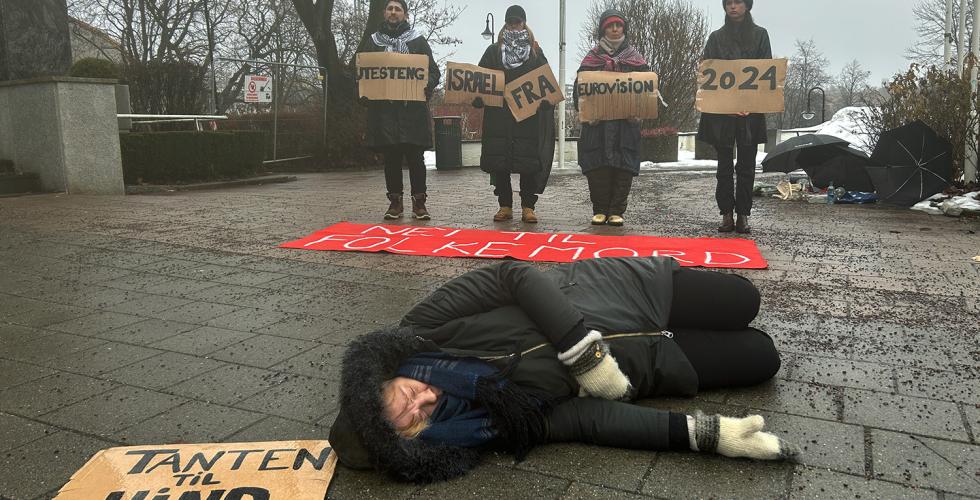 Demonstrant ligger på bakken med et skilt som sier "Tanten til Hind". I bakgrunnen ser man flere demonstranter som holder skilt med budskapet om at Israel må boikottes fra Eurovision.