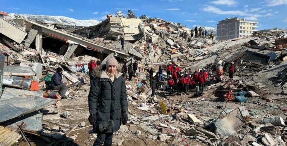 Journalist Åse Marit står i ruinene etter jordskjelvet. Bek henne foregår redningsarbeid. 