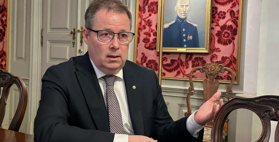 Forsvarsminister Bjørn Aril Gram sitter ved et gammelt trebord med gamle malerier hengende i bakgrunnen. 