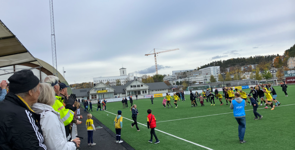 Bilde fra Sandvika Stadion. Bærum sine alagsspillere er stilt opp på rekke, holder hverandre i hendene, og er på vei til å gjøre den såkalte bølgen overfor gjenværende fans på tribunen etter kampen mot Træff.