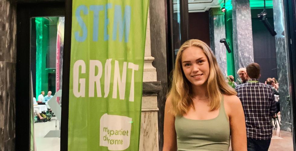 Portrettbilde av Helena Bugge, representant for Grønn ungdom, foran et banner av MDG sin logo, ved valgvaken i Oslo