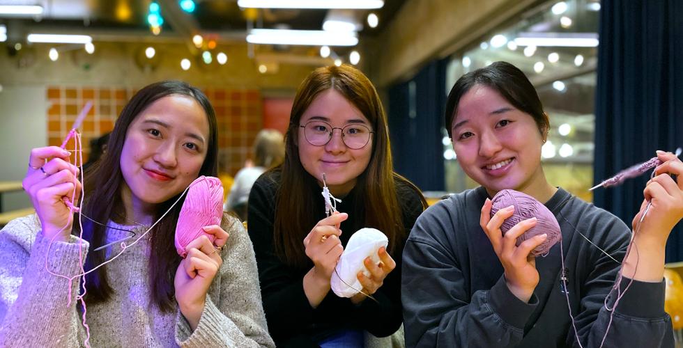 Haruno Eda, Wakana Kawamura og Kak Fung Cheunh smiler til kameraet og viser frem det de har strikket. 