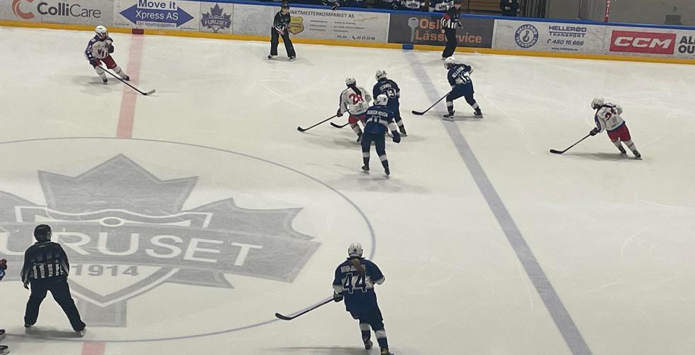 Spillere fra Vålrenga og Furuset spiller ishockey på banen. Spillerne er i bevegelse med ishockeykøller i hånda mens de sender pucken frem og tilbake