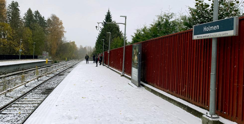 Det snør på Holmen T-banestasjon. Reisende venter på T-banen.