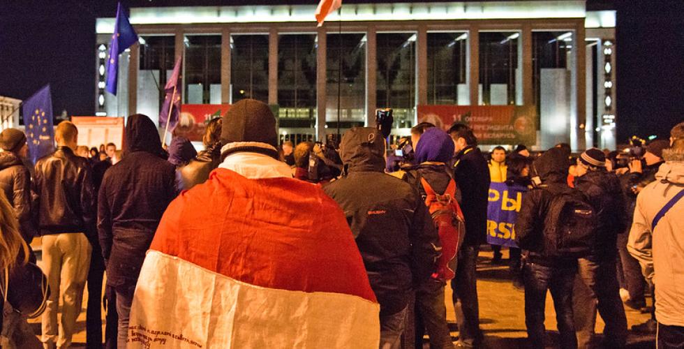 Et kveldsbilde, hvor hviterussiske demonstranter er samlet på et torg og bærer det hvite og røde flagget deres.