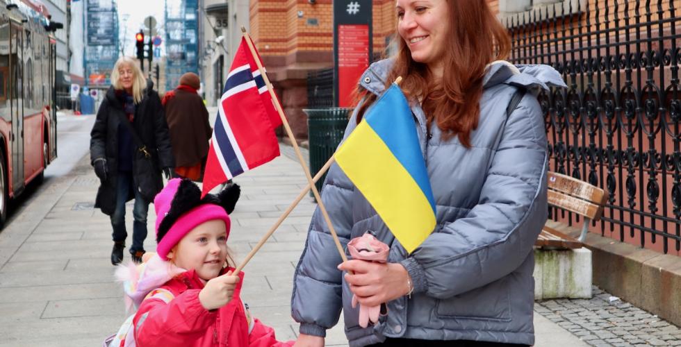 mor og datter på et fortau som holder det norske og det ukrainske flagget i kryss og smiler