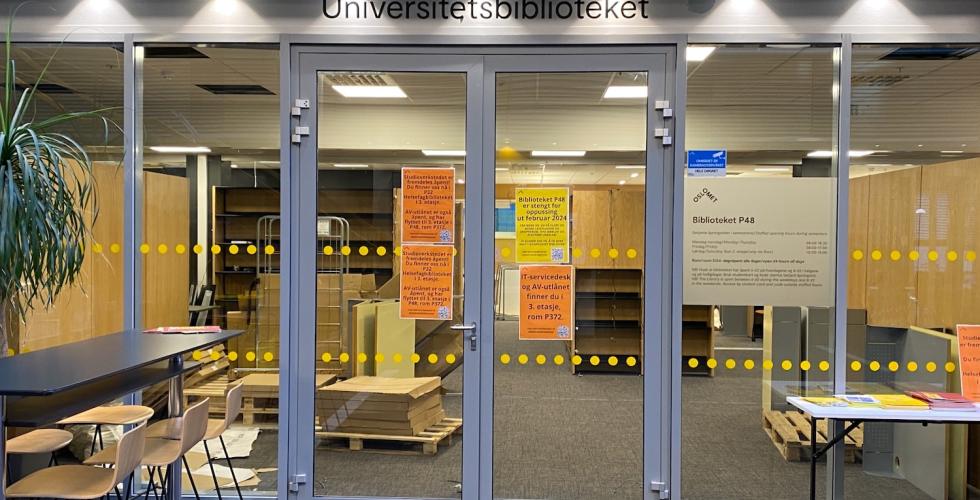 Bildet viser utsiden av biblioteket på P48. Her ser man det henger flere plakater, som handler om at oppussingen kommer til å vare ut februar, og hvor man kan finne hjelp. Igjennom vinduet kan man se at det fortsatt arbeides med montering.