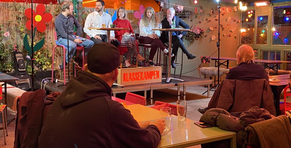 Fem mennesker sitter på en scene og debatterer. 