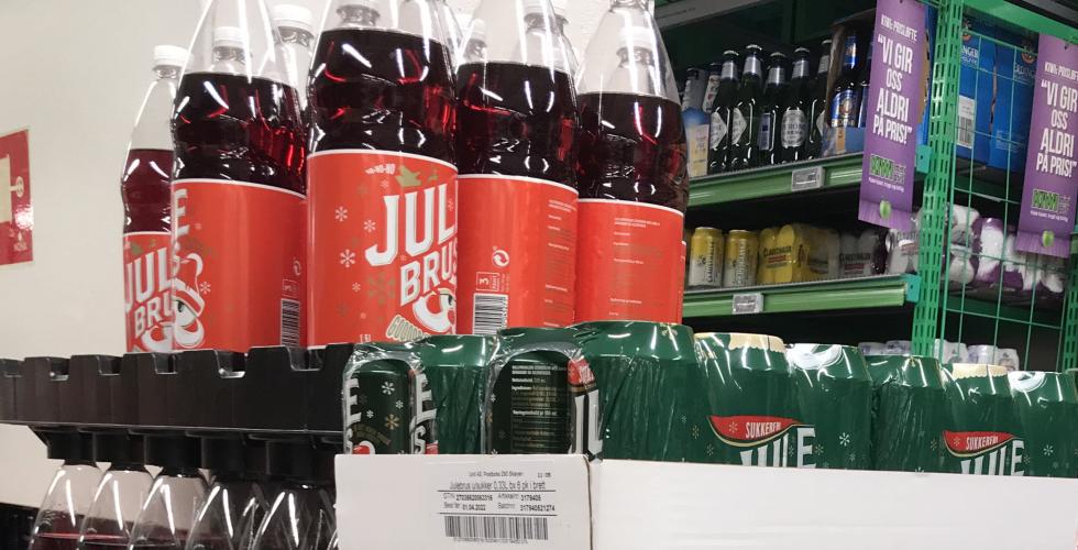 Man ser rød julebrud, og bokser med julebrus, stablet oppå hverandre. 