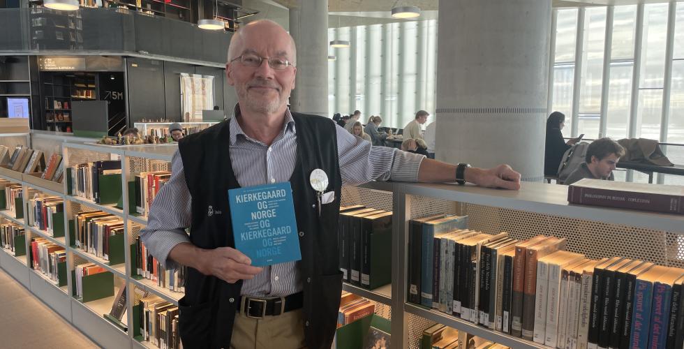 Olav Kapperud poserer foran filosofibøker på Deichman.