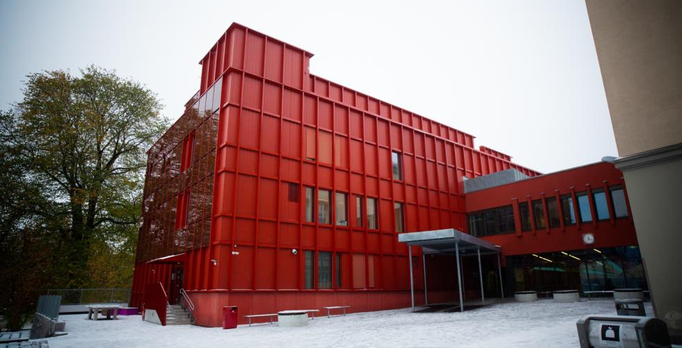 Sofienberg skole fotografert i under en grå himmel. Bygget er farget i en sterk rødfarge. Skolegården er å se i forgrunnen av bildet.