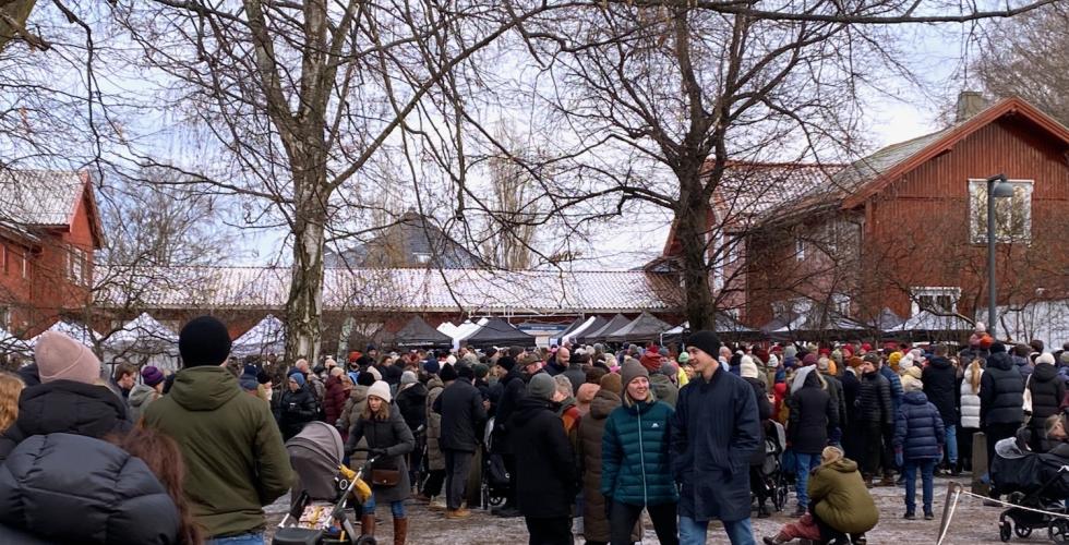 Bildet viser julemarkedet i Botanisk Hage. Det er mange folk som vandrer rundt, og vi kan se taket på bodene bak dem.