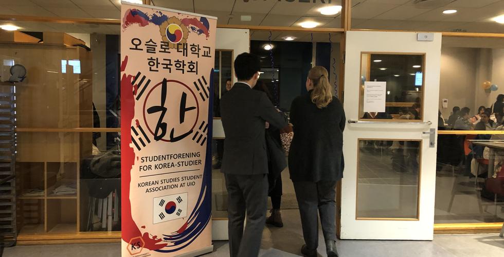 Tre personer går inn døren til en kafeteria. Ved siden av er banneret til Korean Studies Student Association