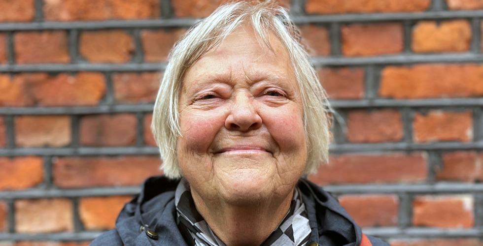 Portrettbilde av Jorunn Chetwynd (76) foran murvegg ved Foss VGS.