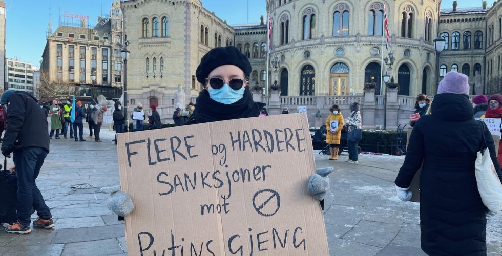 Demonstrant holder et skilt med ordene "flere og hardere sanksjoner mot Putins gjeng" utenfor Stortinget