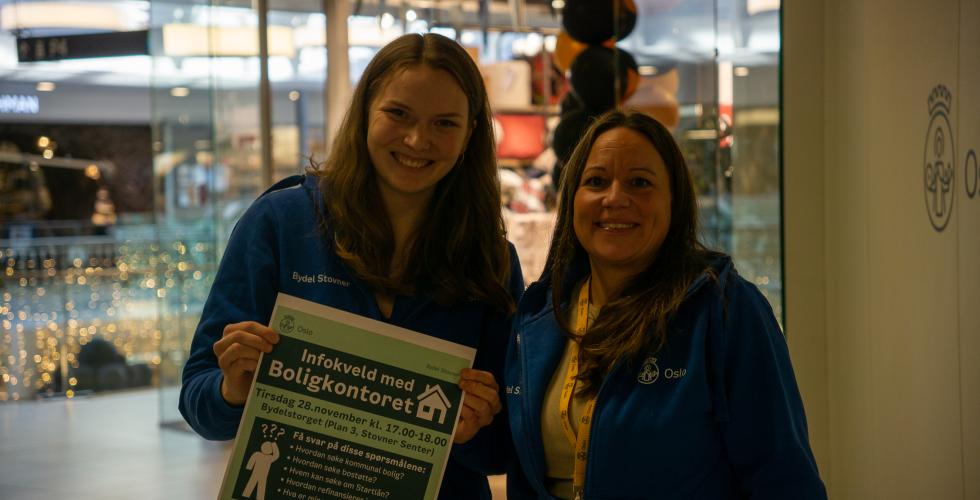 Two women in blue sweaters holding a poster.