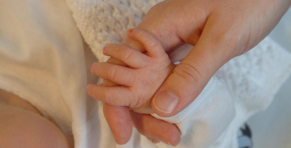 Nyfødt baby holder fingeren til moren. 