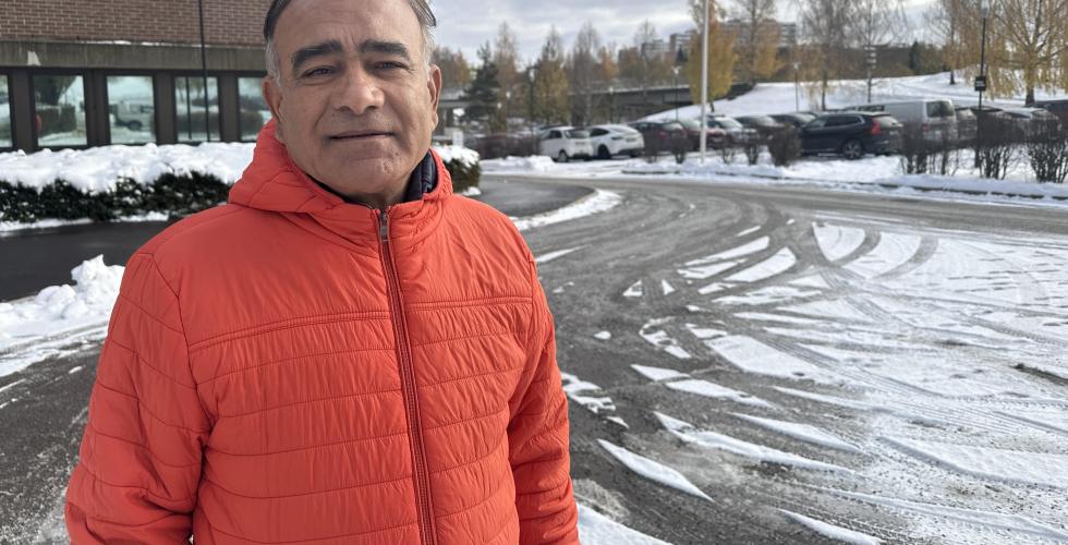 Ombir Singh Upadhyay står i en oransje jakke utenfor et bygg på Stovner i Oslo. 