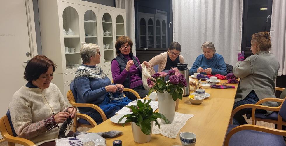 Seks damer på Sagene Frivilligsentral sin strikkekafé, som sitter rundt et bord og drikker kaffe og strikker.