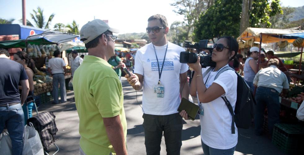 To journalister intervjuer en mann på et travelt marked i Costa Rica. 