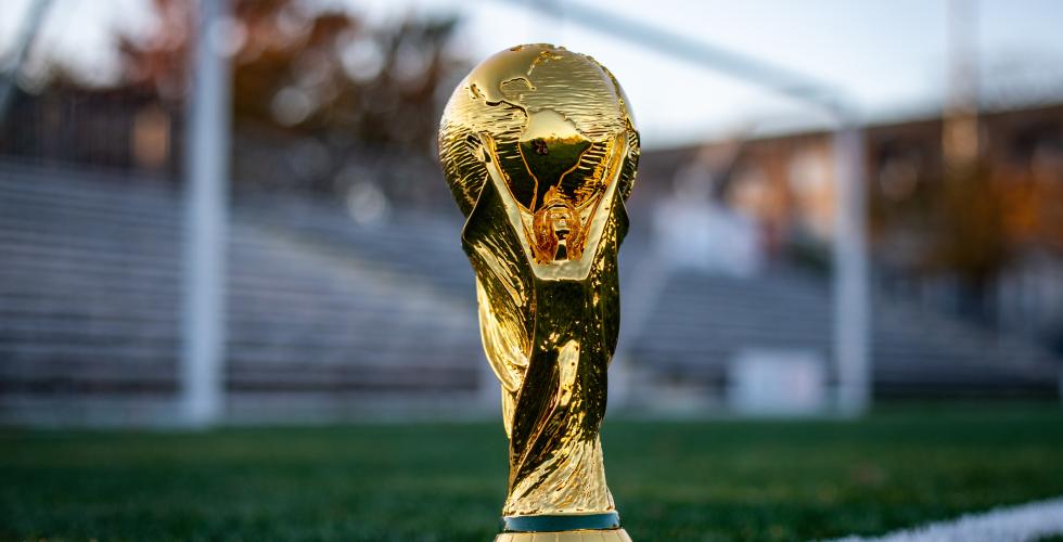 VM-trofeet plassert på toppen av en av de hvite linjene på en fotballbane, med uklar bakgrunn.