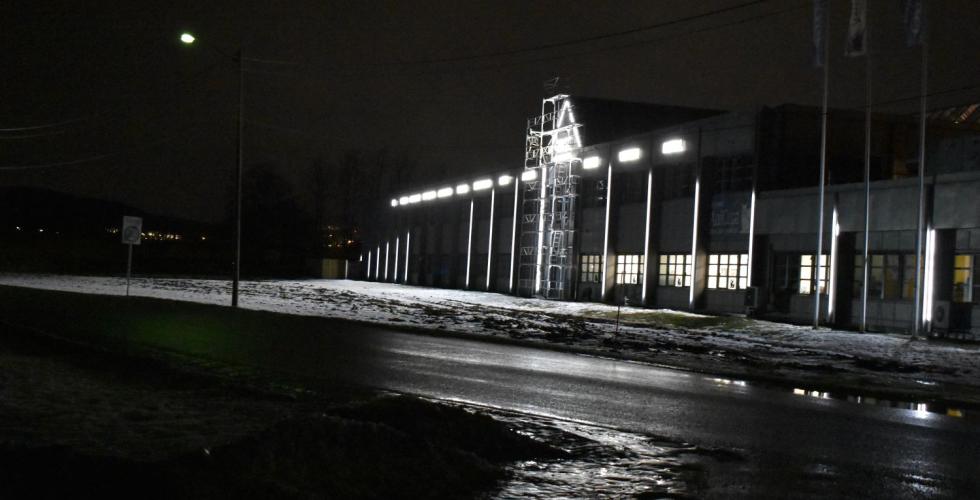 En bygning i en næringspark med logoer lyser opp veien og jordet foran seg. Lysene er hvite og sterke. 