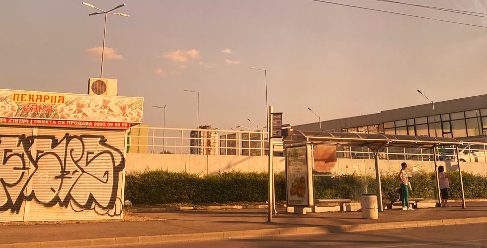 En gate i Bulgaria om sommeren. Det er kun to mennesker på busstoppet.