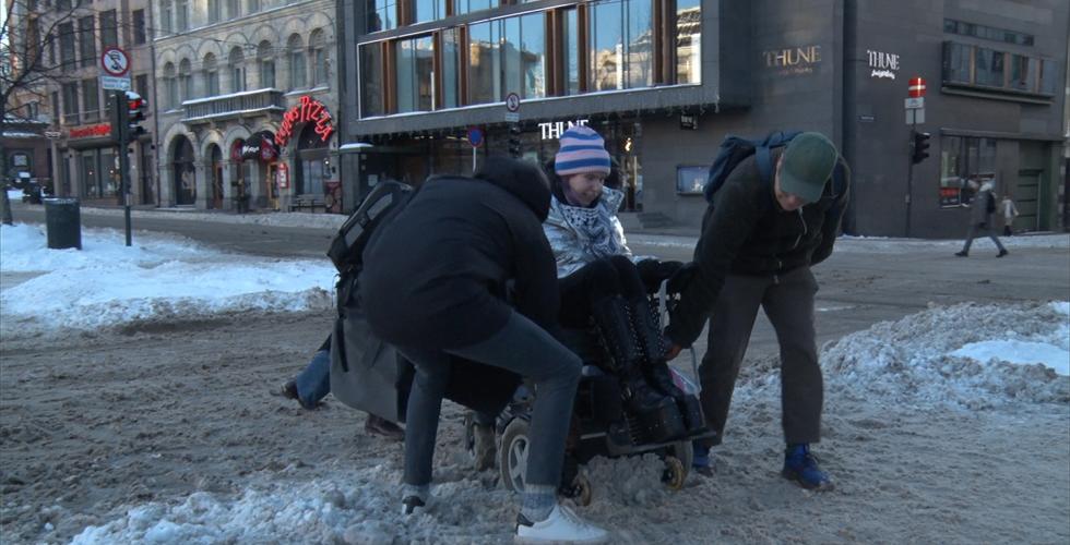 rullestol sitter fast i snø i Oslo, to personer hjelper