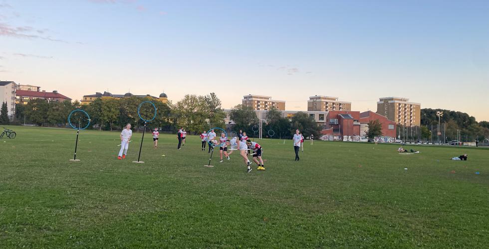 Gressplen hvor to lag spiller mot hverandre i rumpeldunk. Alle spillerne har en stikke mellom beina. 