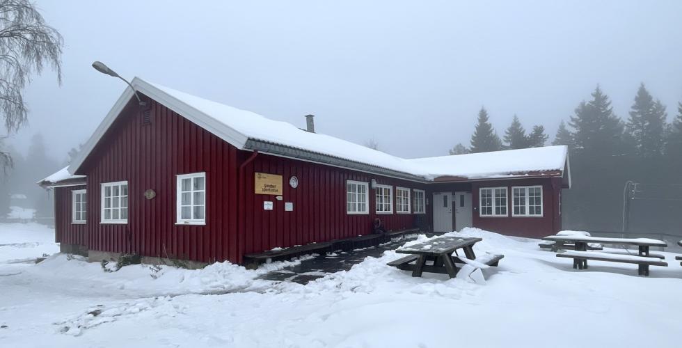 En rød hytte med lys snø på tak og omkring