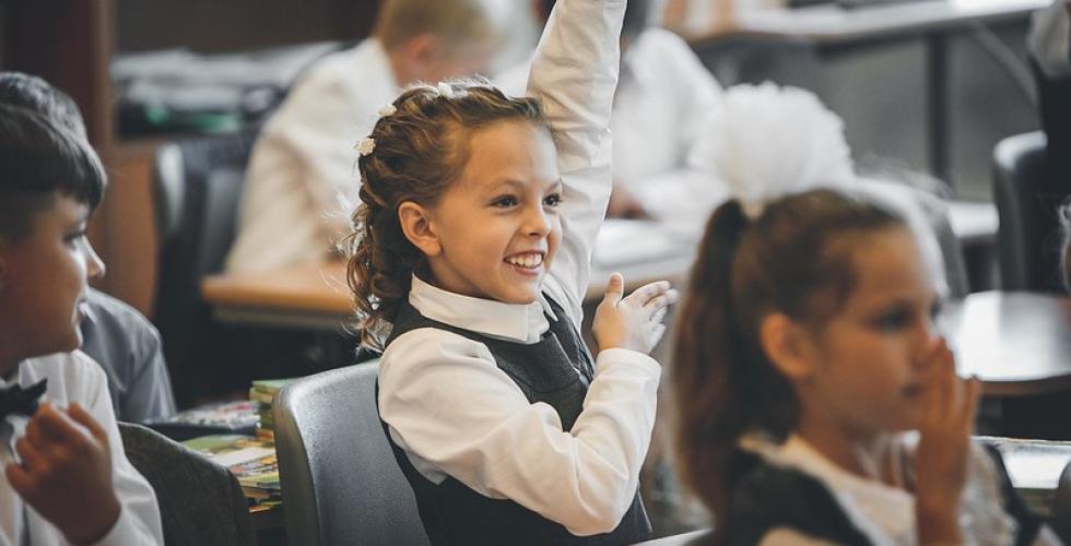 smilende skolepike rekker opp hånden i klasserommet