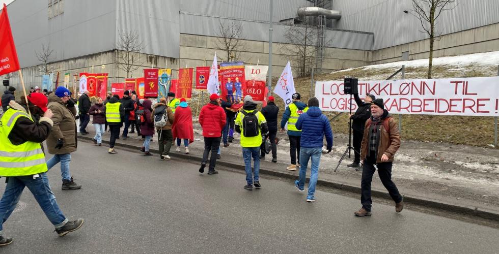 Mennesker går over veien, skilt og bannere i bakgrunnen