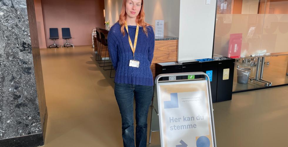 Valgmedarbeider Sunniva Harstein står bak en plakat med teksten "Her kan du stemme".