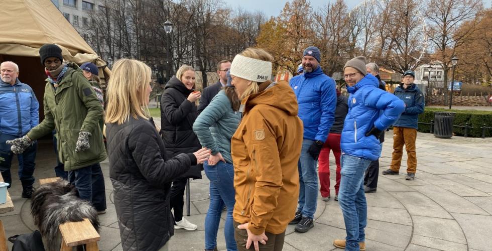 Politikere og representanter fra Norsk Friluftsliv står samlet utenfor Stortinget ved en lavo og et bord med kaffe og gløgg. 