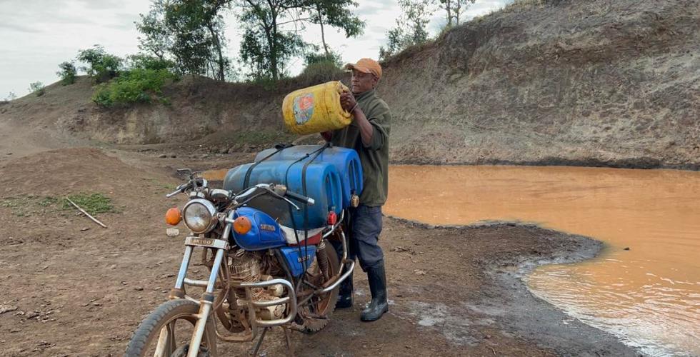 Bilde av en mann i Afrika som samler skittent vann i plastdunker fra en bekk