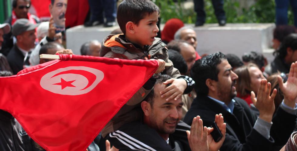 Barn som sitter på farens skuldre med et tunisisk flagg