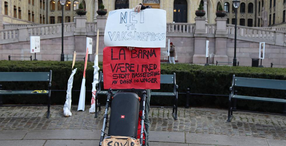 En demonstrant fra Røde Luer skjuler seg bak plakater mot vaksinepass