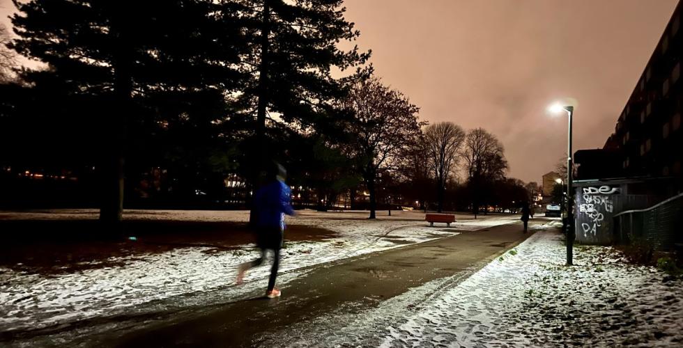 Det er mørkt ute og mann jogger forbi på en vei med snø