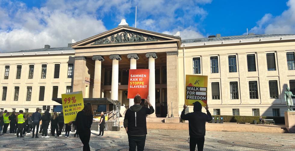 Tre personer står med ryggen til og viser plakater