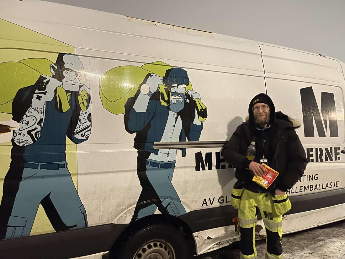 Mann står smilende ved firmabilen til Medarbeiderne