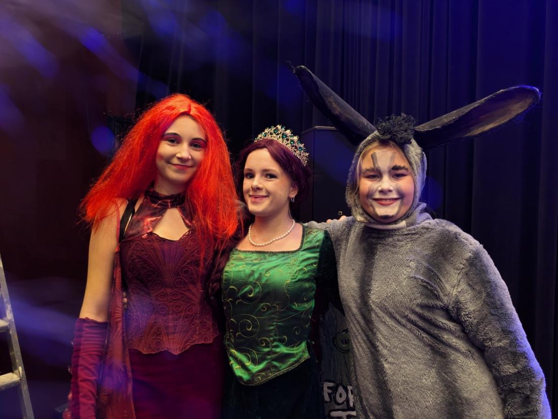 Tre jenter som smiler til kamera, utkledd som karakterene Dragen, Fiona og Esel fra Shrek